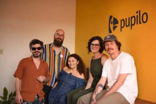 Equipe da Pupilo em frente ao painel amarelo com o logo